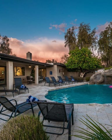 Backyard pool with lounge chairs and rock waterfall at dusk