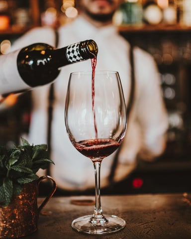 Bartender pouring red wine into a glass at a warmly lit bar